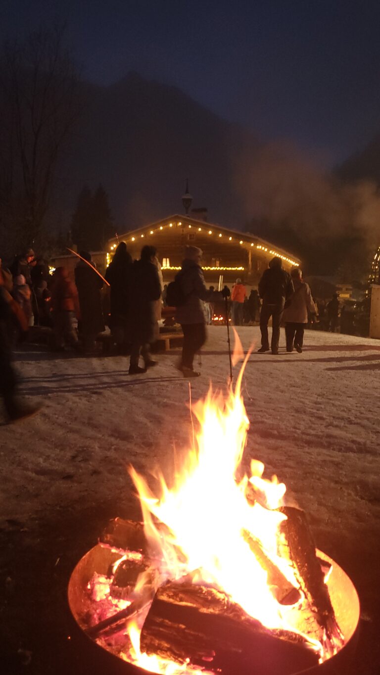 Stimmung am Gelände des Arlerhofes, Menschen im Hintergrund und Lagerfeuer im Vordergrund.