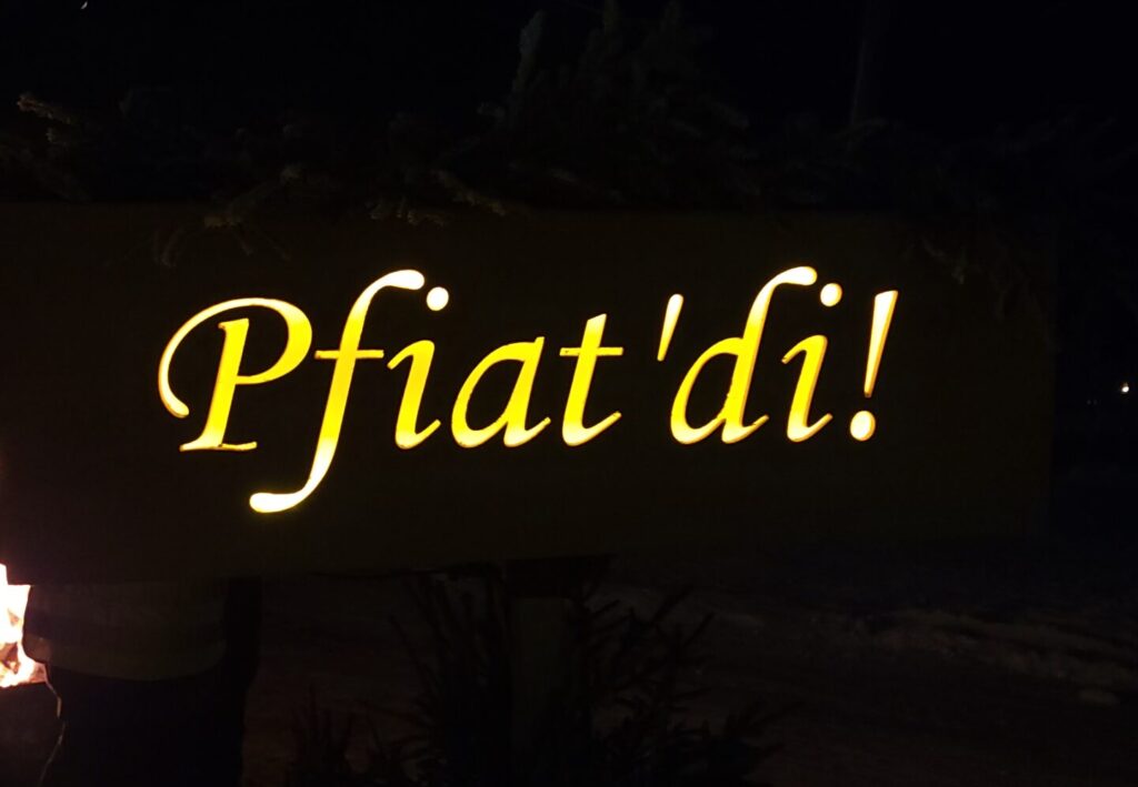 Leuchtendes Pfiat'di Schild in der Dunkelheit als herzliche Verabschiedung von der Weihnachtsroas in Abtenau.